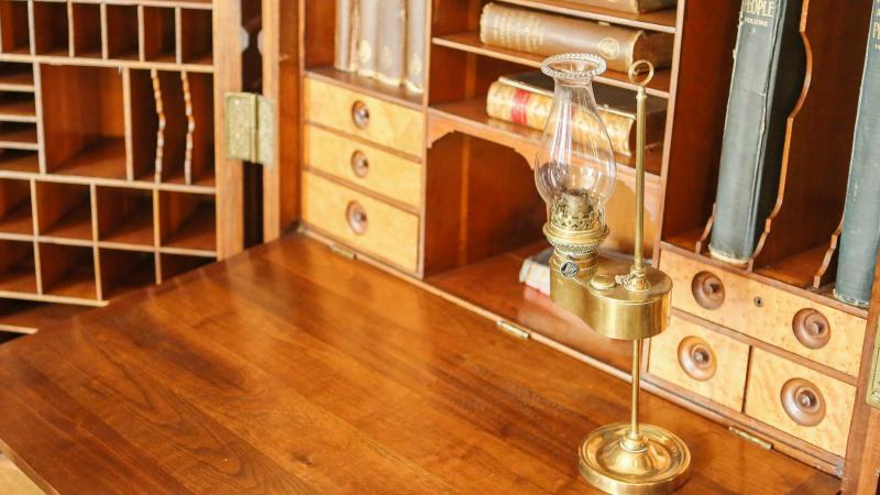 Antique wooden desk with open compartments and an oil lamp.