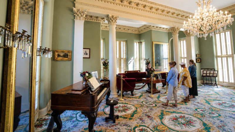 Elegant room with chandelier, piano, and people admiring decor.