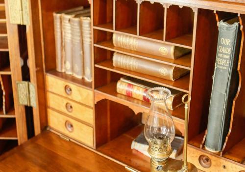 Antique wooden desk with books and an ornate oil lamp.