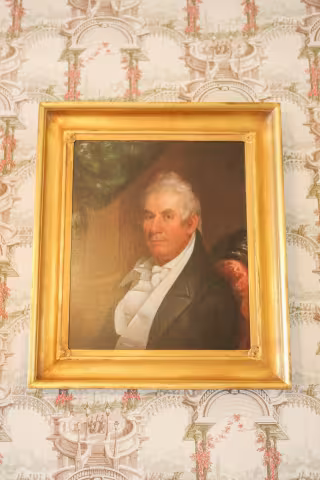 Portrait of a man in a gold frame on patterned wallpaper.
