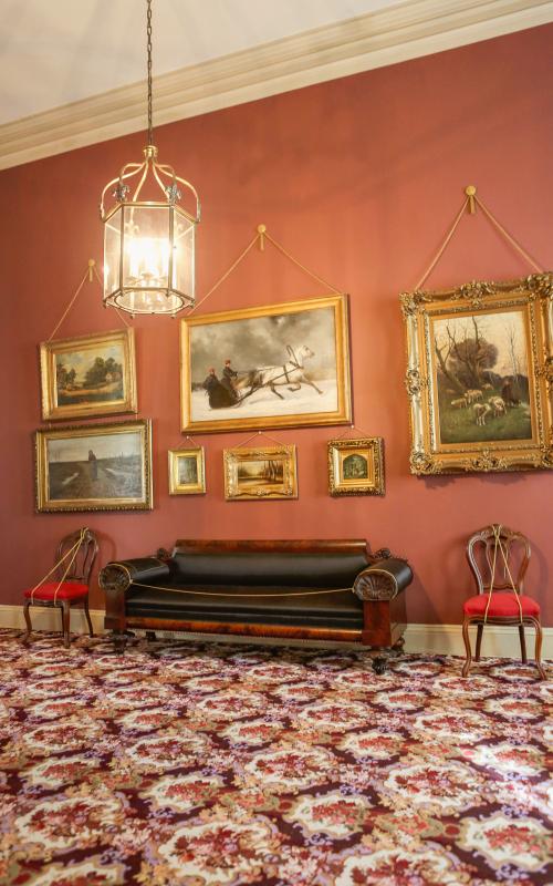 Ornate room with red walls, paintings, antique sofa, and patterned carpet.